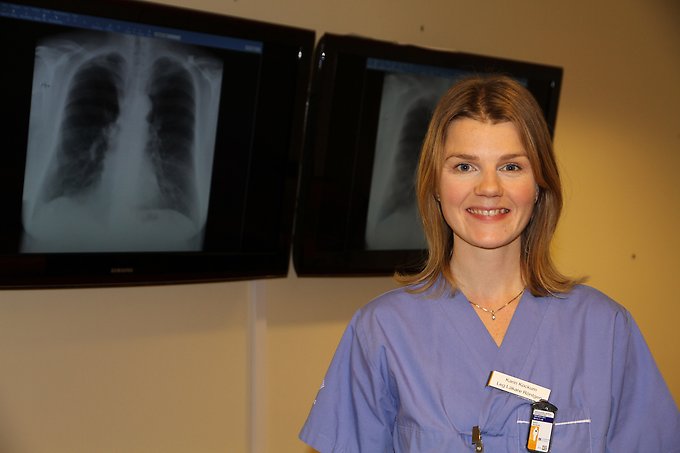 porträtt på en kvinnlig läkare iklädd blå vårdkläder stående framför en röntgenbild av lungor