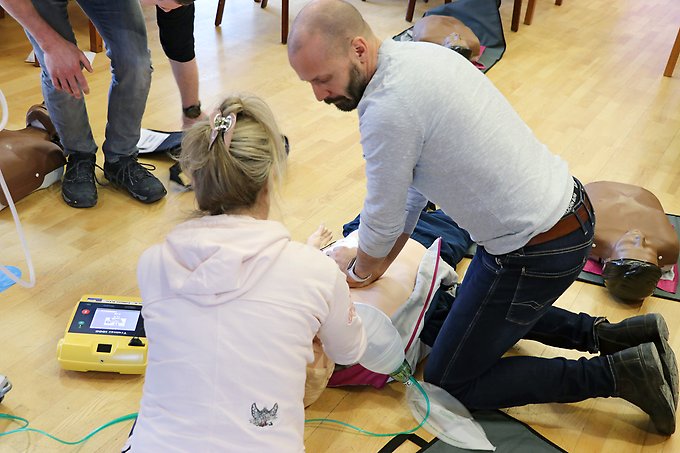 tre personer övar på hjärt- och lungräddning med en defibrillator på en övningsdocka