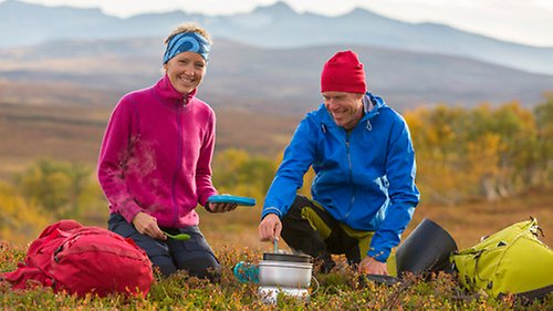 Två personer sitter på ett fjäll och lagar mat i ett stormkök.