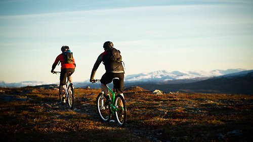 Två personer cyklar i fjällmiljö.