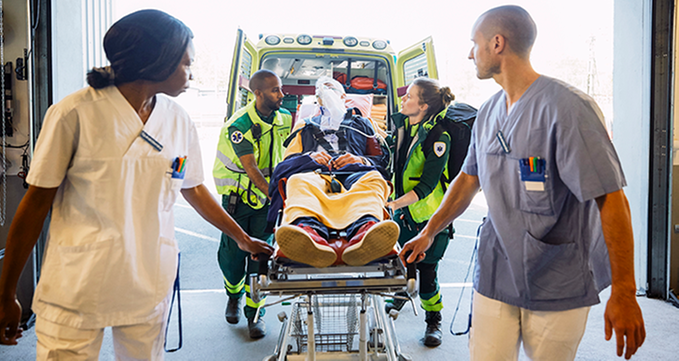 En bår med en patient rullas ut ur en ambulans av två ambulansförare, och tas emot av vårdpersonal på sjukhuset. Foto: Maskot Bildbyrå AB/Johnér