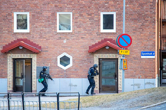 två insatspoliser med gevär smyger intill fasaden på en skola
