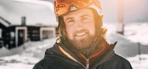 Porträttbild på en person i skidhjälm, i solig och snöig vintermiljö.