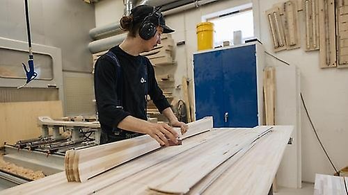 Fabriksarbetare står vid arbetsbänk och jobbar med en hög beskurna träplankor som ska bli till skidor. Foto: Tobias Liljeroth