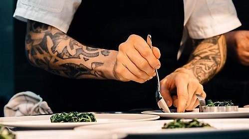 En kocks händer lägger upp portioner av avsmakningsmeny på tallrikar.