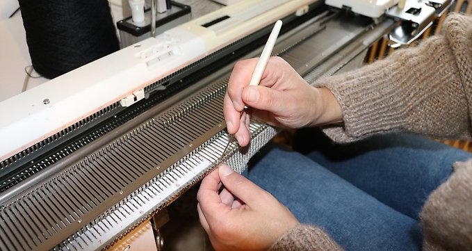 Ett par händer hanterar nålar och tråd vid en handstickningsmaskin. Foto: Region Jämtland Härjedalen